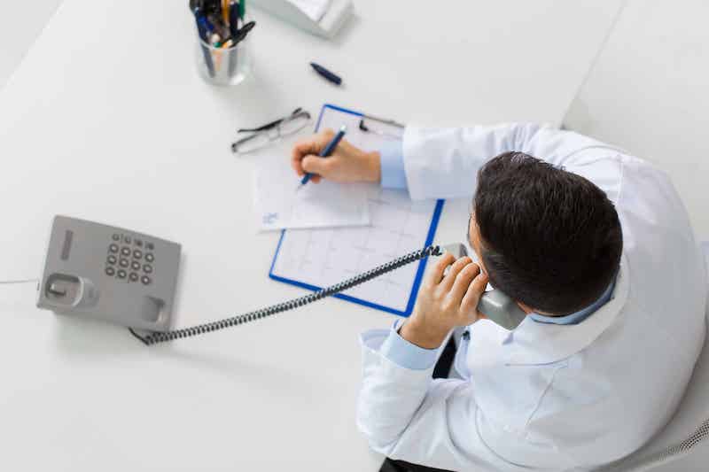 Doctor talking on phone and writing on paper 