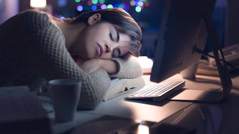 Woman sleeping in front of computer with her head on her desk