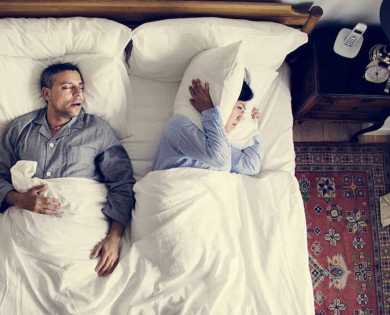 Woman holding her ears while man sleeps and snores